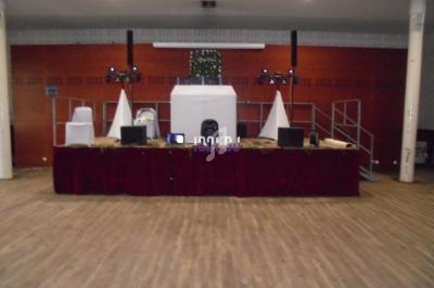 Installation d'une scène avec table recouverte de tissu rouge, matériel audio et éclairage dans une salle au sol en bois.