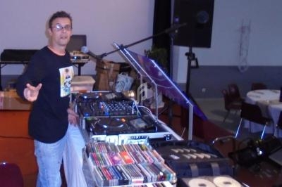 Un DJ devant une table de mixage avec des platines, des CD et des cassettes dans une salle équipée de matériel audio.