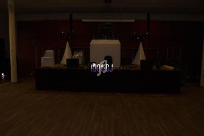 Scène sombre avec une installation de matériel audio et éclairage, dans une salle vide au sol en parquet.