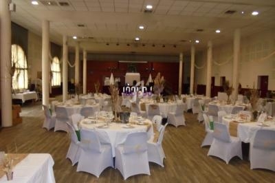 Salle de réception décorée avec des tables rondes dressées, nappes blanches et chaises assorties, éclairage naturel.
