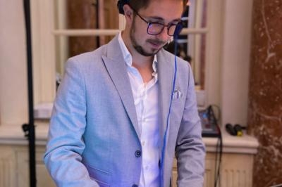 Un homme en costume clair mixe de la musique sur une console DJ dans un intérieur élégant.