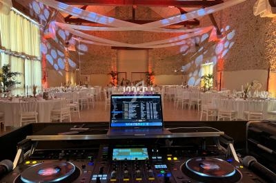Salle de réception décorée avec des tables dressées, vue depuis une console de DJ équipée de platines et d'un ordinateur.