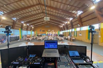 Vue depuis une table de mixage sur une grande salle décorée, avec des tables dressées pour un événement.