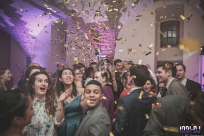 Groupe de personnes souriantes dans une fête, sous une pluie de confettis dorés, dans une salle voûtée éclairée.