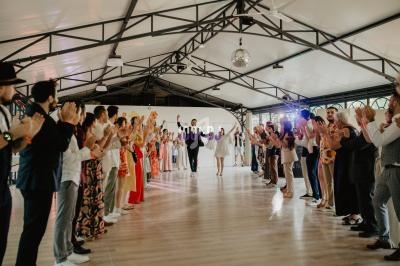 Des invités applaudissent un couple dansant au centre d'une salle lumineuse avec une structure métallique.