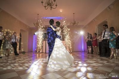 Un couple danse au centre d'une salle éclairée par des projecteurs et des étincelles, entouré d'invités.