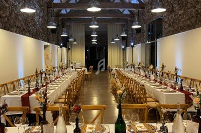 Salle de réception avec deux longues tables dressées, décorées de fleurs, bougies et vaisselle élégante.