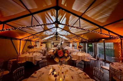 Salle de réception décorée avec des guirlandes lumineuses, des tables rondes dressées et des compositions florales.