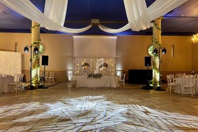 Salle de réception décorée avec des drapés blancs suspendus, colonnes illuminées et piste de danse éclairée.