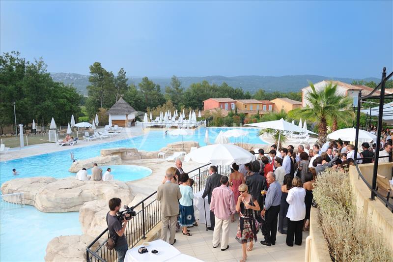 Groupe de personnes rassemblées près d'une piscine extérieure entourée de parasols et de végétation.