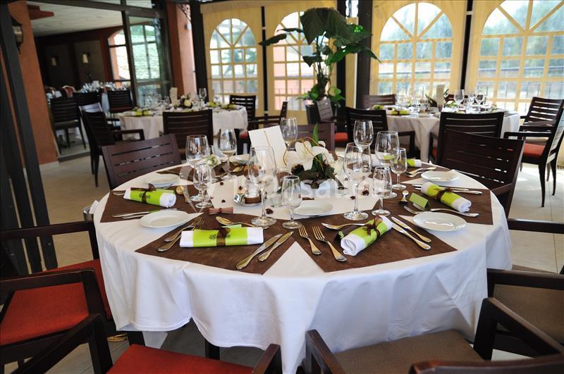 Table dressée pour un repas élégant avec nappes blanches, serviettes vertes, vaisselle et verres dans une salle lumineuse.