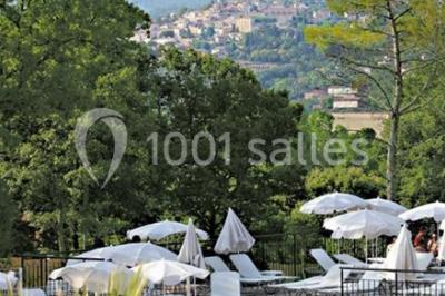 Salle d'attente lumineuse avec fauteuils en rotin, coussins clairs, tables basses et plantes vertes sur un tapis rouge.