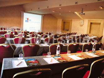 Salle de conférence équipée de tables, chaises, bouteilles d'eau, blocs-notes et projecteur allumé.