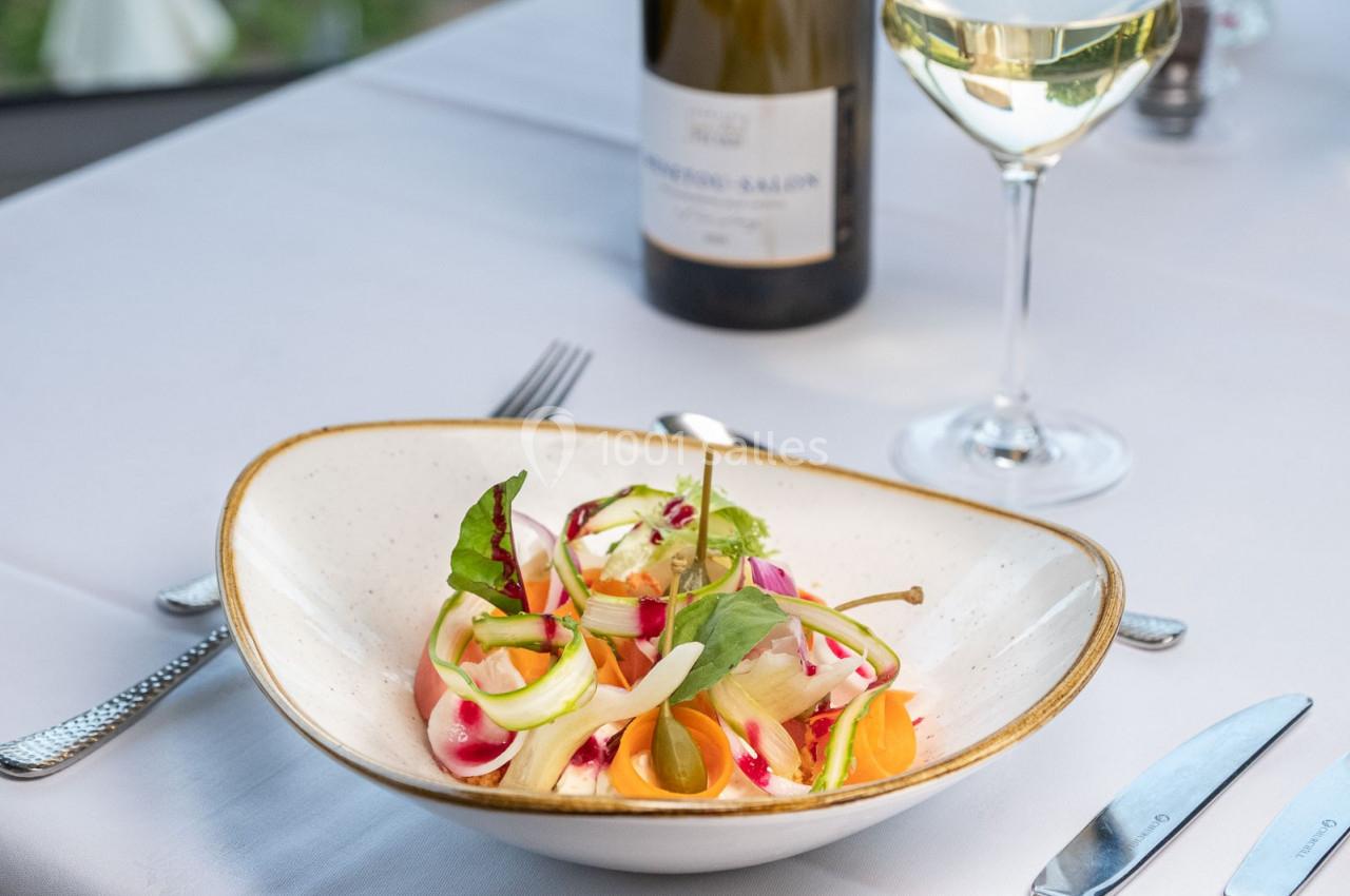 Assiette de salade colorée avec légumes frais, servie sur une table dressée avec un verre de vin blanc et une bouteille.