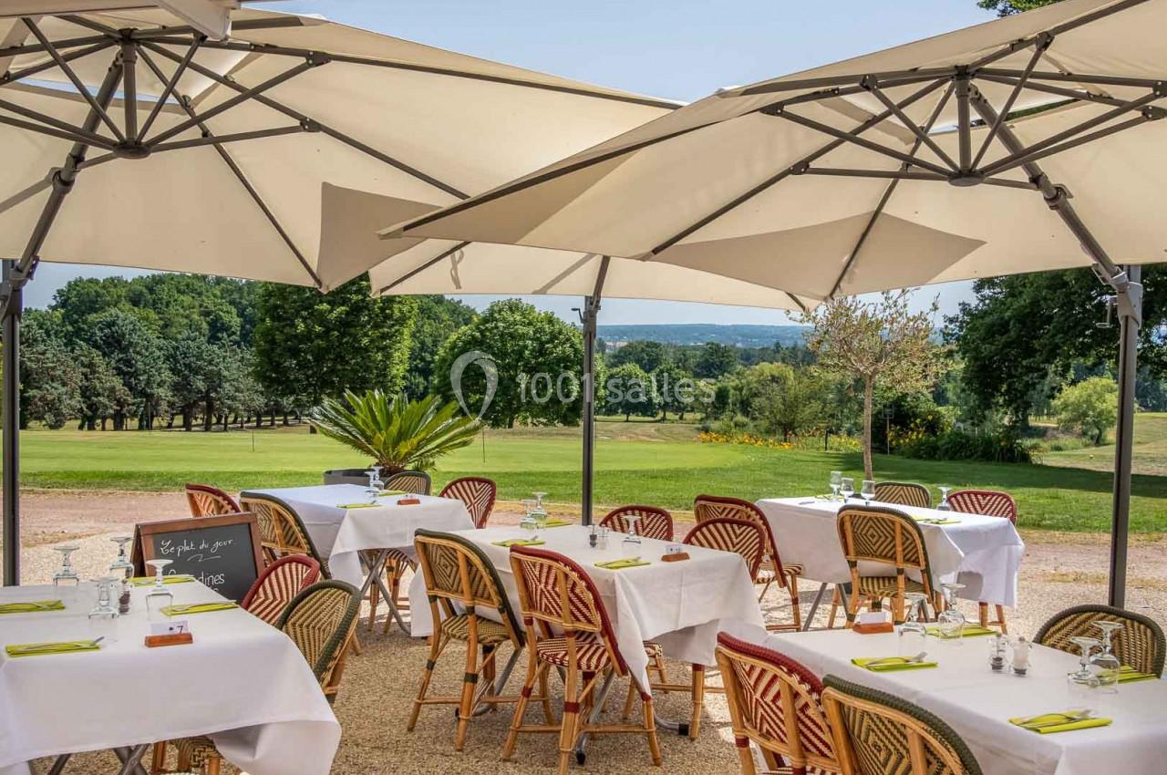 Terrasse d'un restaurant avec tables dressées sous des parasols, offrant une vue sur un paysage verdoyant.