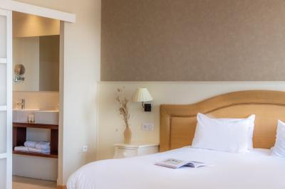 Chambre lumineuse avec un lit double, une table de chevet, une lampe et une salle de bain attenante visible en arrière-plan.