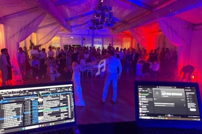Un couple danse devant une foule dans une salle éclairée de lumières colorées, vue depuis une table de DJ.
