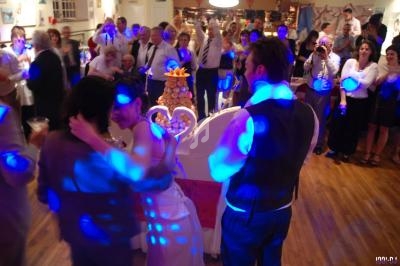 Groupe de personnes célébrant un mariage autour d'une pièce montée dans une salle éclairée par des lumières colorées.