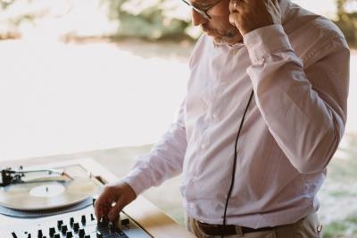Un homme écoute un casque tout en mixant des disques vinyles sur une table de mixage en extérieur.