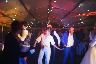 Des personnes dansent sous une tente éclairée par des guirlandes lumineuses lors d'un événement festif.