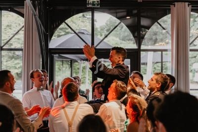 Un homme en costume est porté par un groupe de personnes applaudissant dans une salle avec de grandes fenêtres.