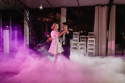 Un couple danse au milieu d'une piste enveloppée de fumée et éclairée par des lumières roses dans une salle élégante.