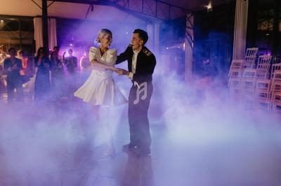 Un couple danse au milieu d'une piste enveloppée de fumée, sous des lumières violettes, devant des spectateurs.