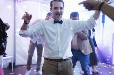 Un homme en chemise blanche et nœud papillon danse sous des lumières colorées dans une ambiance festive.