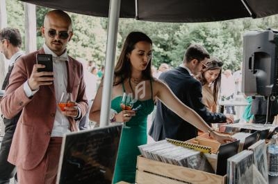 Des personnes autour d'une table de DJ en extérieur, avec des vinyles, un tourne-disque et des boissons à la main.