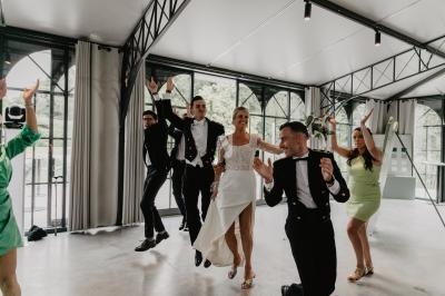 Un groupe de personnes élégamment vêtues danse joyeusement dans une salle lumineuse avec de grandes fenêtres.