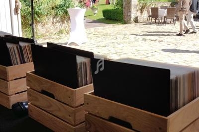 Des caisses en bois contenant des disques vinyles sur une table, avec un jardin et des invités en arrière-plan.