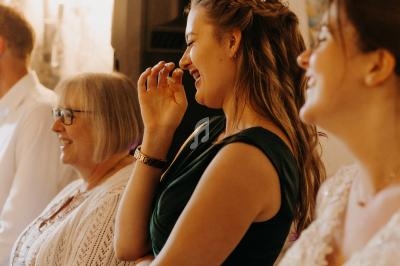 Des personnes souriantes debout dans une pièce éclairée, dont une femme en robe verte riant discrètement.