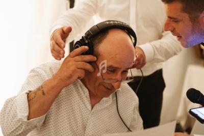 Un homme portant un casque audio lit un document, entouré de deux personnes souriantes dans un cadre intérieur.