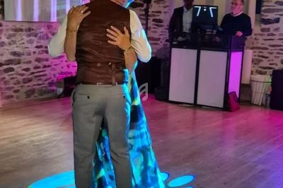 Un couple danse dans une salle en pierre éclairée par des lumières colorées, avec un DJ en arrière-plan.