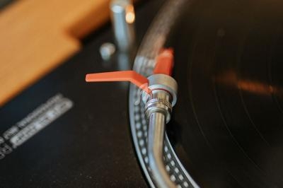 Bras de lecture d'une platine vinyle posée sur un disque noir, avec un fond en bois clair.