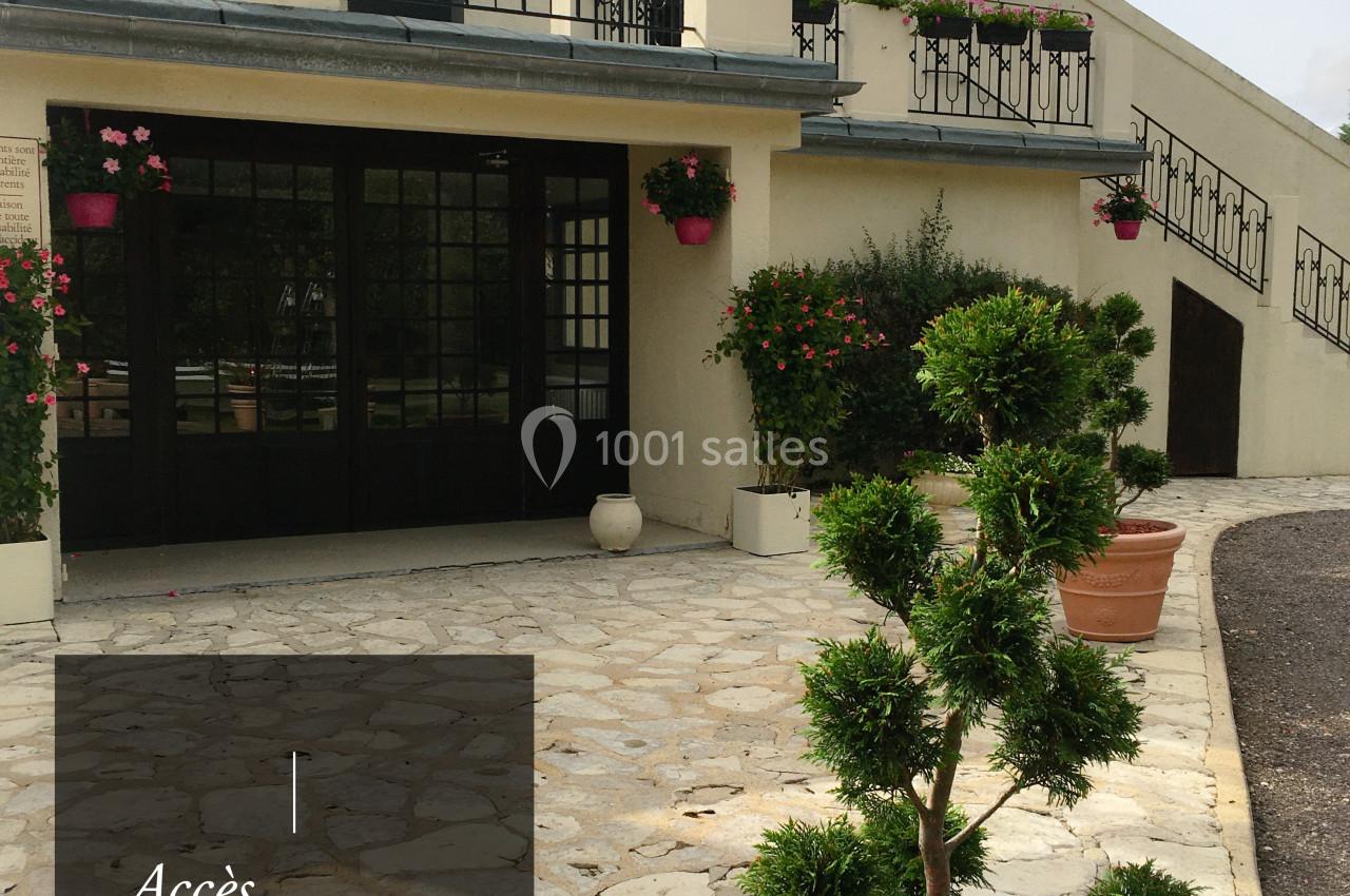Accès extérieur à un bâtiment avec terrasse fleurie, escalier et arbuste taillé en pot au premier plan.