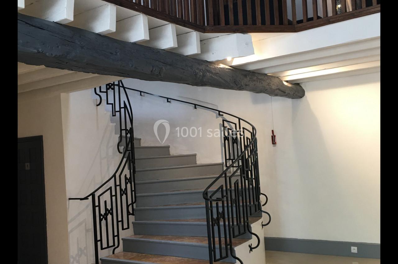 Escalier en colimaçon avec garde-corps en métal menant à une mezzanine en bois dans une salle lumineuse.