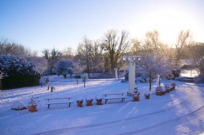 Paysage hivernal avec jardin enneigé, arbres dénudés et soleil bas illuminant la scène.