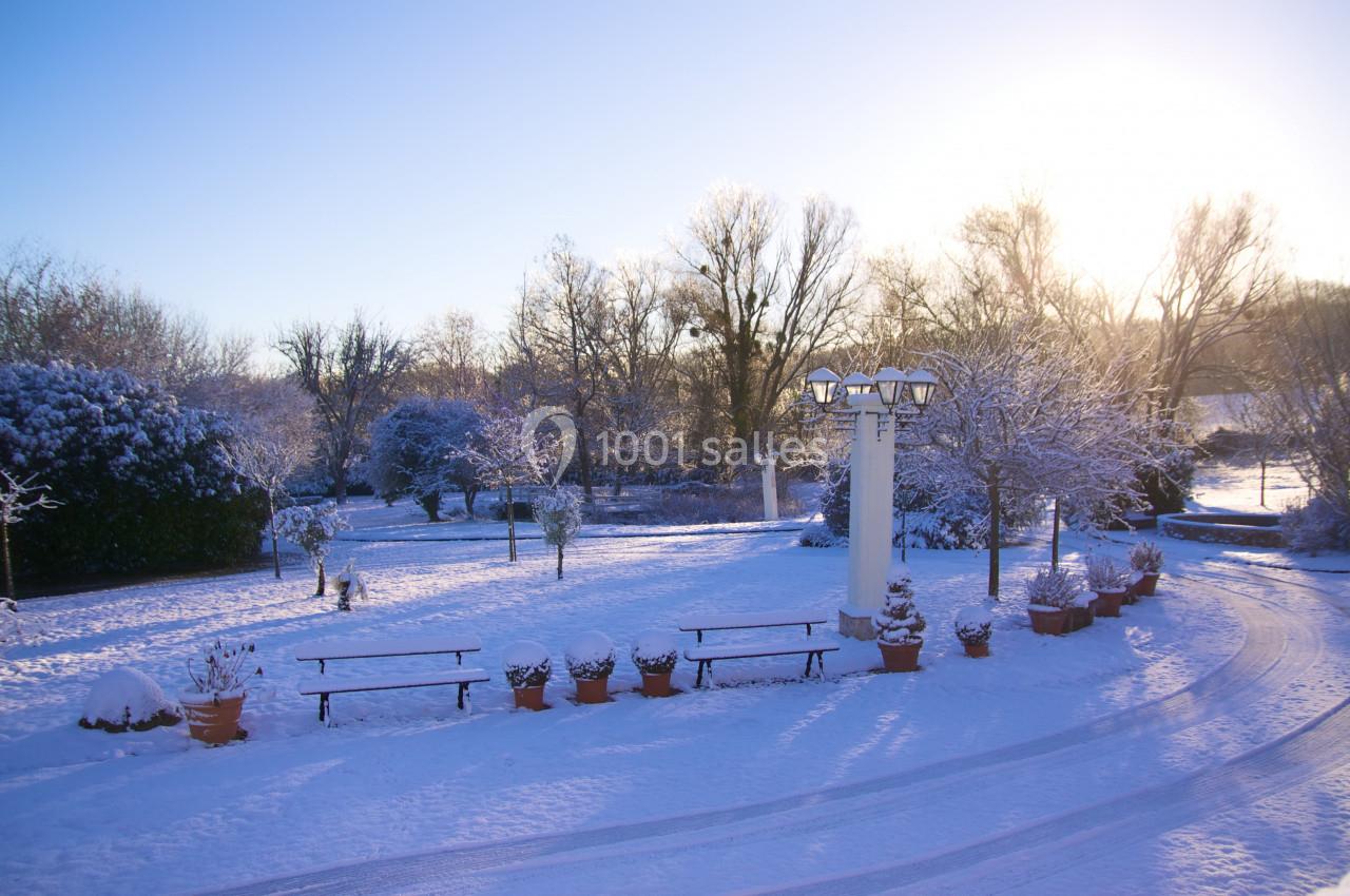 Jardin enneigé au lever du soleil, avec bancs, pots de fleurs et arbres recouverts de neige.