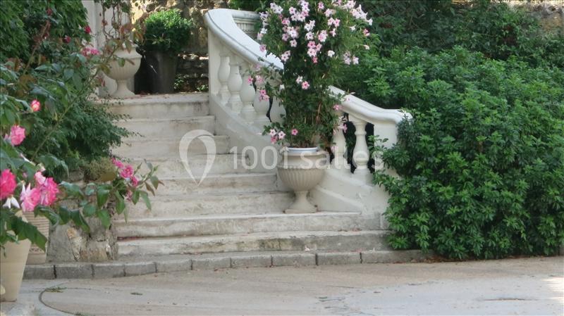 Escalier en pierre bordé de balustrades blanches, entouré de plantes et de fleurs roses dans un jardin.
