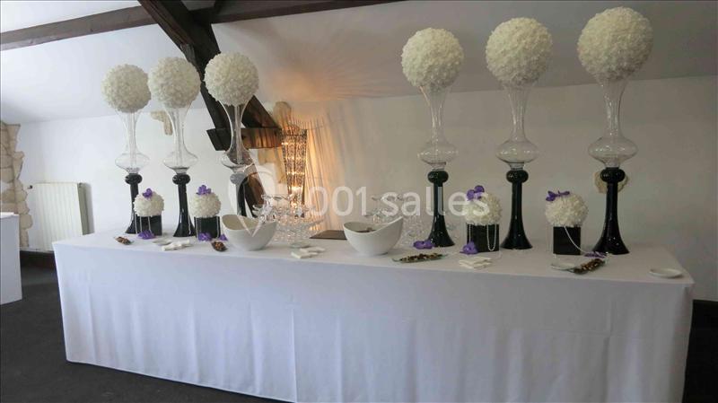 Table décorée avec des vases hauts contenant des boules de fleurs blanches, bols et verres disposés dans une salle lumineuse.