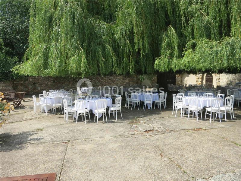 Tables rondes dressées avec nappes blanches et chaises disposées en extérieur sous des saules pleureurs.