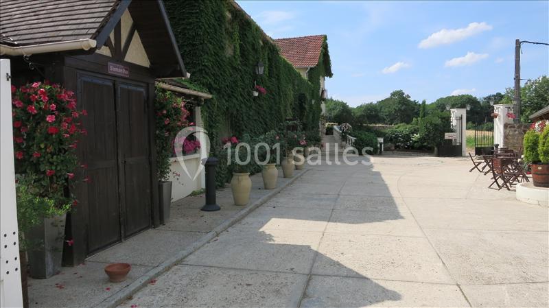 Cour pavée bordée de bâtiments avec murs recouverts de lierre, pots de fleurs et mobilier de jardin en bois.