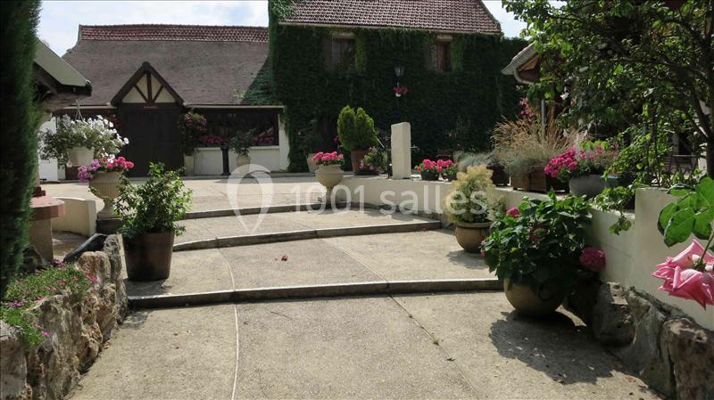 Allée en béton bordée de pots de fleurs menant à une maison avec façade couverte de lierre.