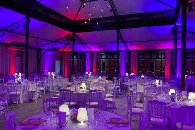 Salle de réception lumineuse avec des invités assis à des tables rondes sous un éclairage violet.