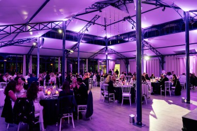 Salle de réception lumineuse avec des invités assis à des tables rondes sous un éclairage violet.