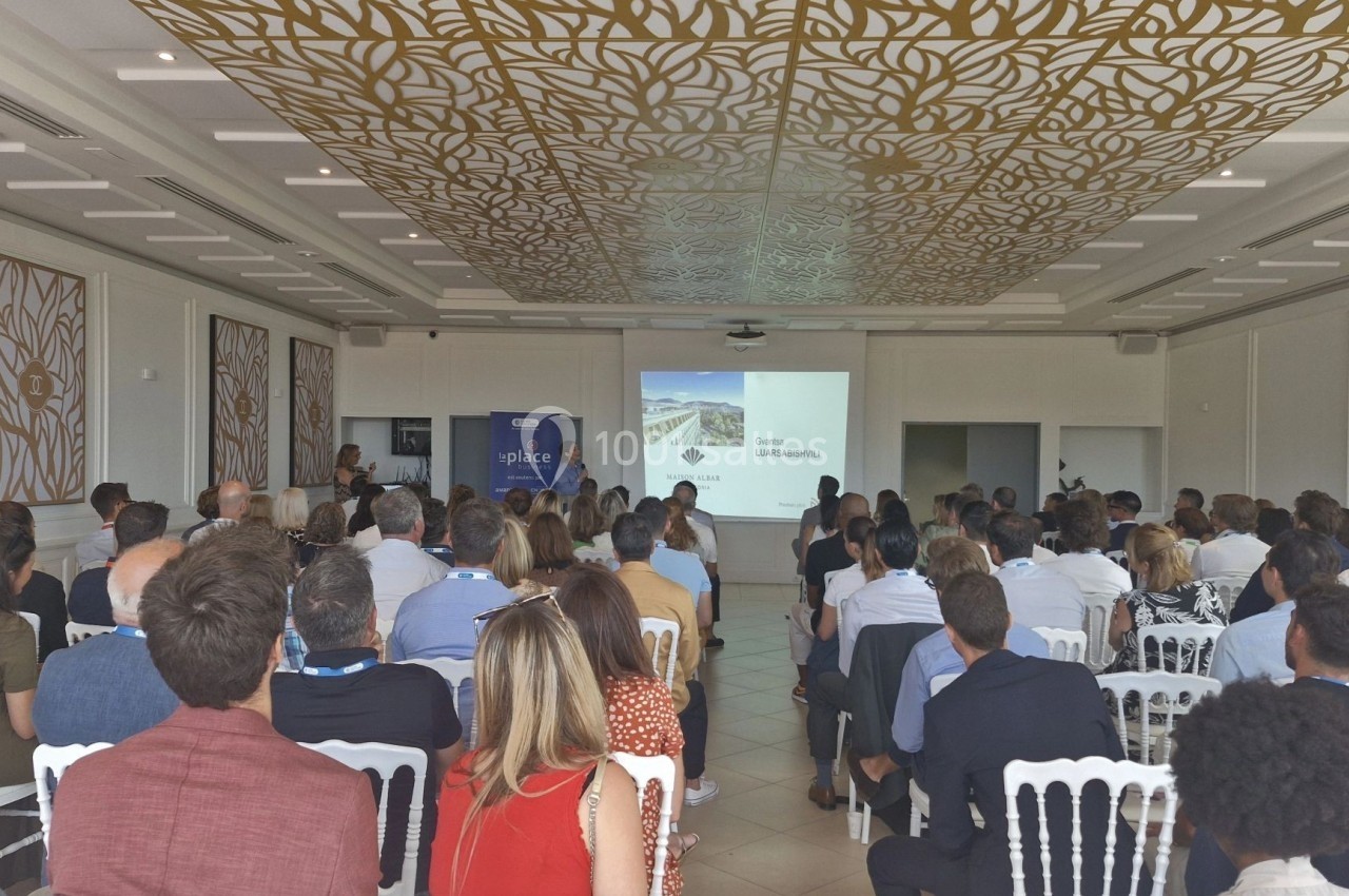 Salle de conférence avec des participants assis, regardant une présentation projetée sur un écran.
