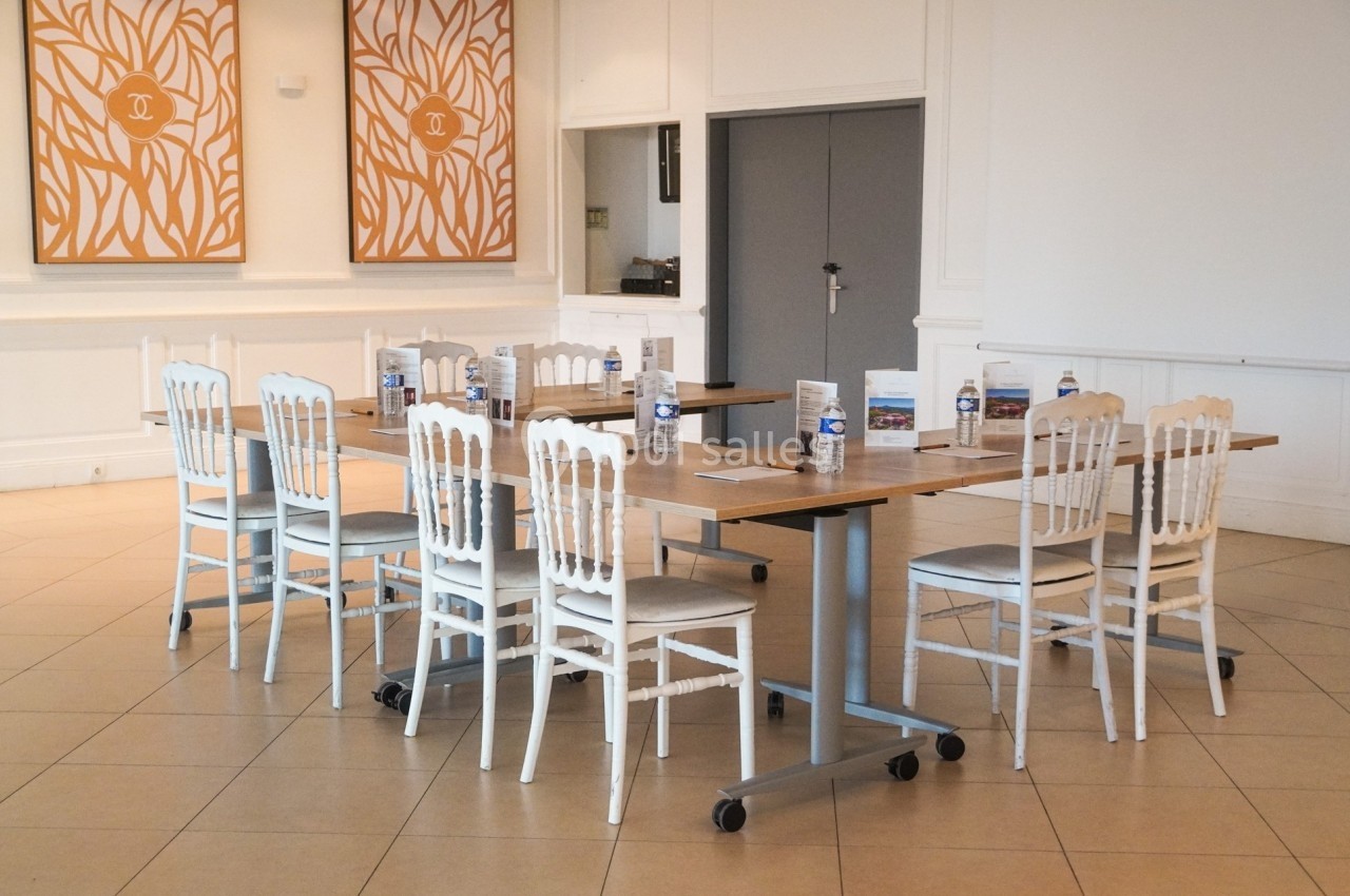 Table rectangulaire avec chaises blanches, disposée dans une salle lumineuse avec décorations murales orange.
