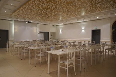 Salle de réception lumineuse avec des invités assis à des tables rondes sous un éclairage violet.