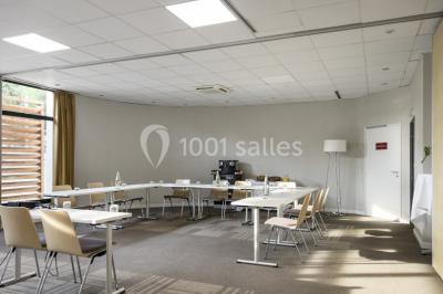 Salle lumineuse avec table en bois, chaises modernes, coin salon, lit double et murs aux tons neutres et bleu.